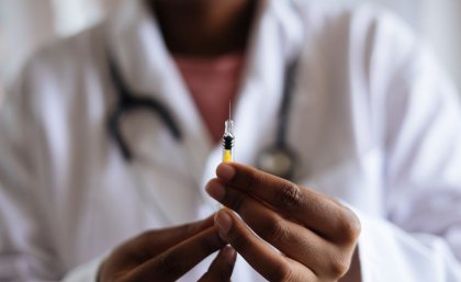 Physician in white coat holding a syringe containing vaccine